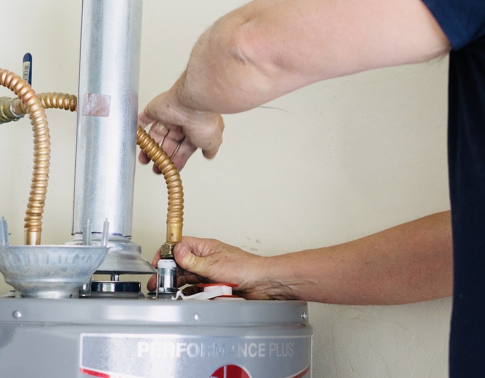 Adult male using a wrench to make adjustments on top of a hot water heater Adult male using a wrench to make adjustments on top of a hot water heater