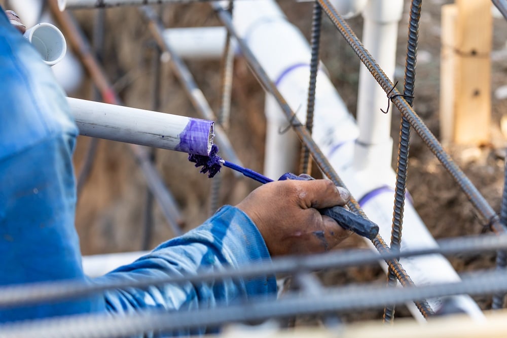 Plumber Applying Pipe Cleaner, Primer and Glue to PVC Pipe At Construction Site.