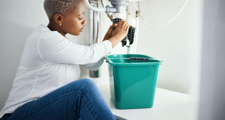 Plumbing, leak and a black woman in the bathroom of her home with a cloth and bucket waiting for as.