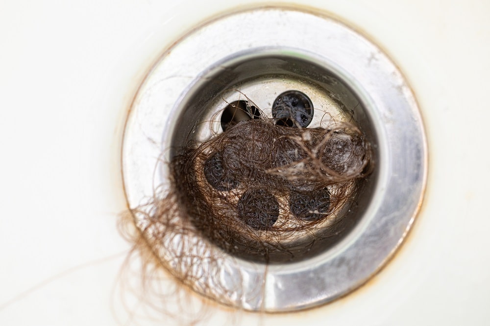 Close-up. Bathroom drain is clogged with dark human hair. Means for cleaning pipes and plumbing. 