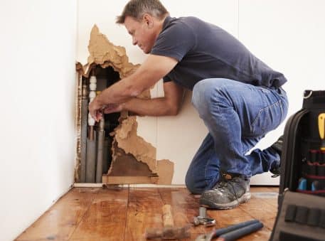Middle aged man repairing burst water pipe