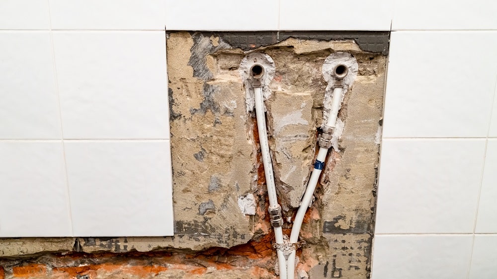 old water supply to faucet in bathroom and plumbing with metal-plastic pipes in chiseled brick wall under removed ceramic tiles