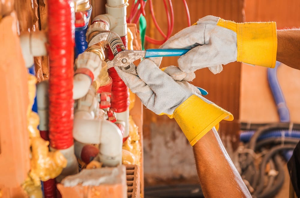Plumber Finishing Whole New Water Supply System Inside Concrete Blocks Build Commercial Building. Close Up on His Hands.
