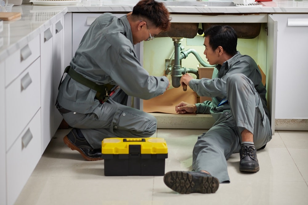 Plumbers installing new plastic pipes under kitchen sink