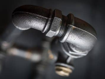 Close-up of a black metal plumbing pipe with an elbow joint against a dark, blurred background, illustrating details that can help explain why pipe burst incidents might occur.