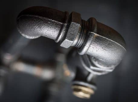 Close-up of a black metal plumbing pipe with an elbow joint against a dark, blurred background, illustrating details that can help explain why pipe burst incidents might occur.