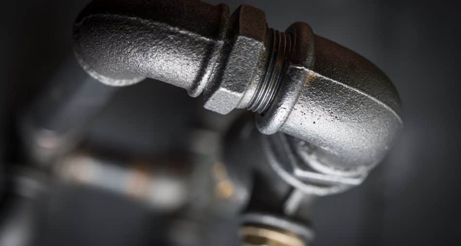 Close-up of a black metal plumbing pipe with an elbow joint against a dark, blurred background, illustrating details that can help explain why pipe burst incidents might occur.