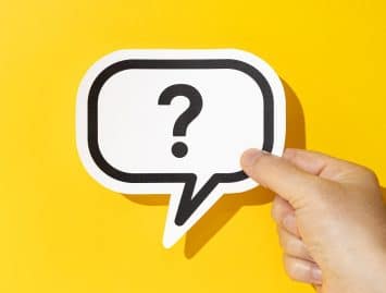 Hand holding a question mark on speech bubble on yellow background. Doubt, confusion, uncertainty concept