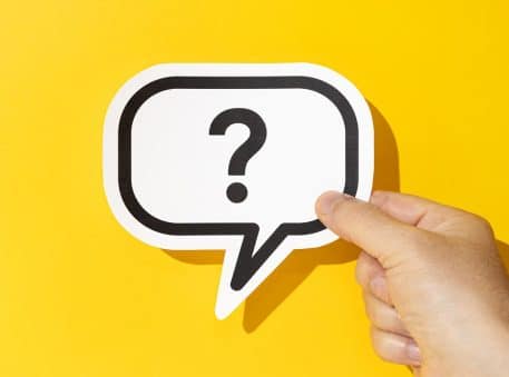 Hand holding a question mark on speech bubble on yellow background. Doubt, confusion, uncertainty concept