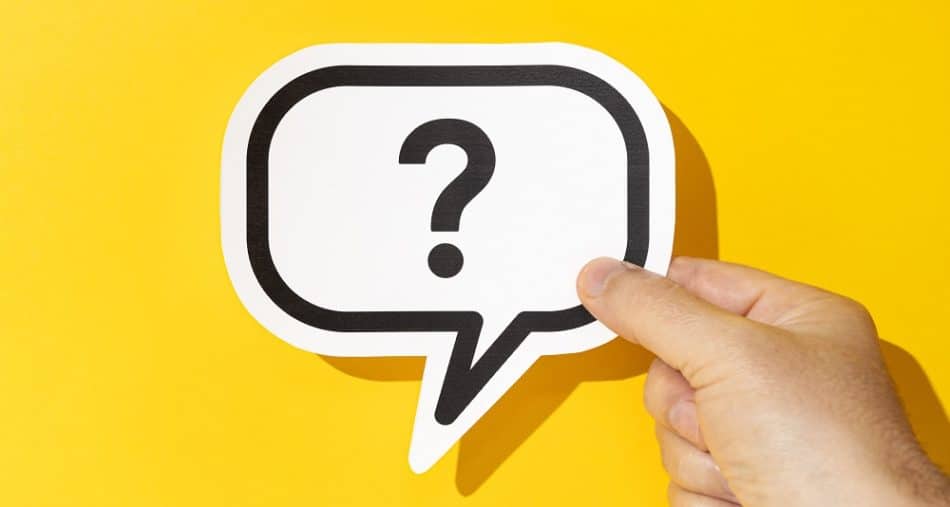 Hand holding a question mark on speech bubble on yellow background. Doubt, confusion, uncertainty concept