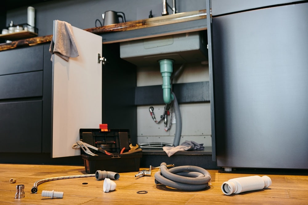 Open door of cabinet under sink in the kitchen, toolbox and plumbing equipment