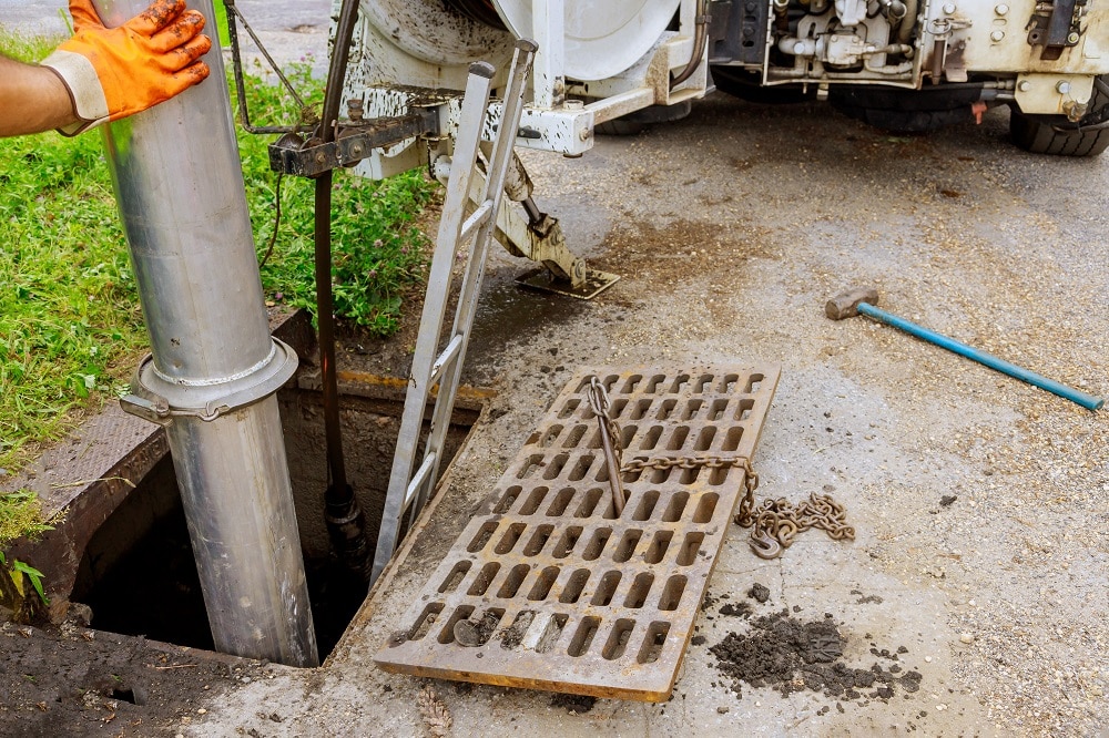 A worker in orange gloves operates a large vacuum hose to clean a storm drain, showcasing the thorough approach of Sewer Inspection Services in New Orleans, with a metal grate and tools placed on the ground nearby.