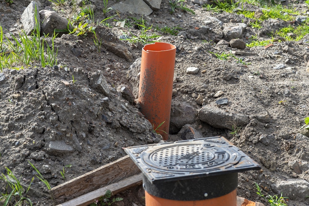 Orange drainage pipe and drain cover installed in a dirt area with rocks and grass, part of an outdoor construction or landscaping project—highlighting the benefits of regular sewer inspections for maintaining proper drainage.